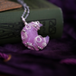 Pink, rose quartz crescent moon necklace on a purple fabric background