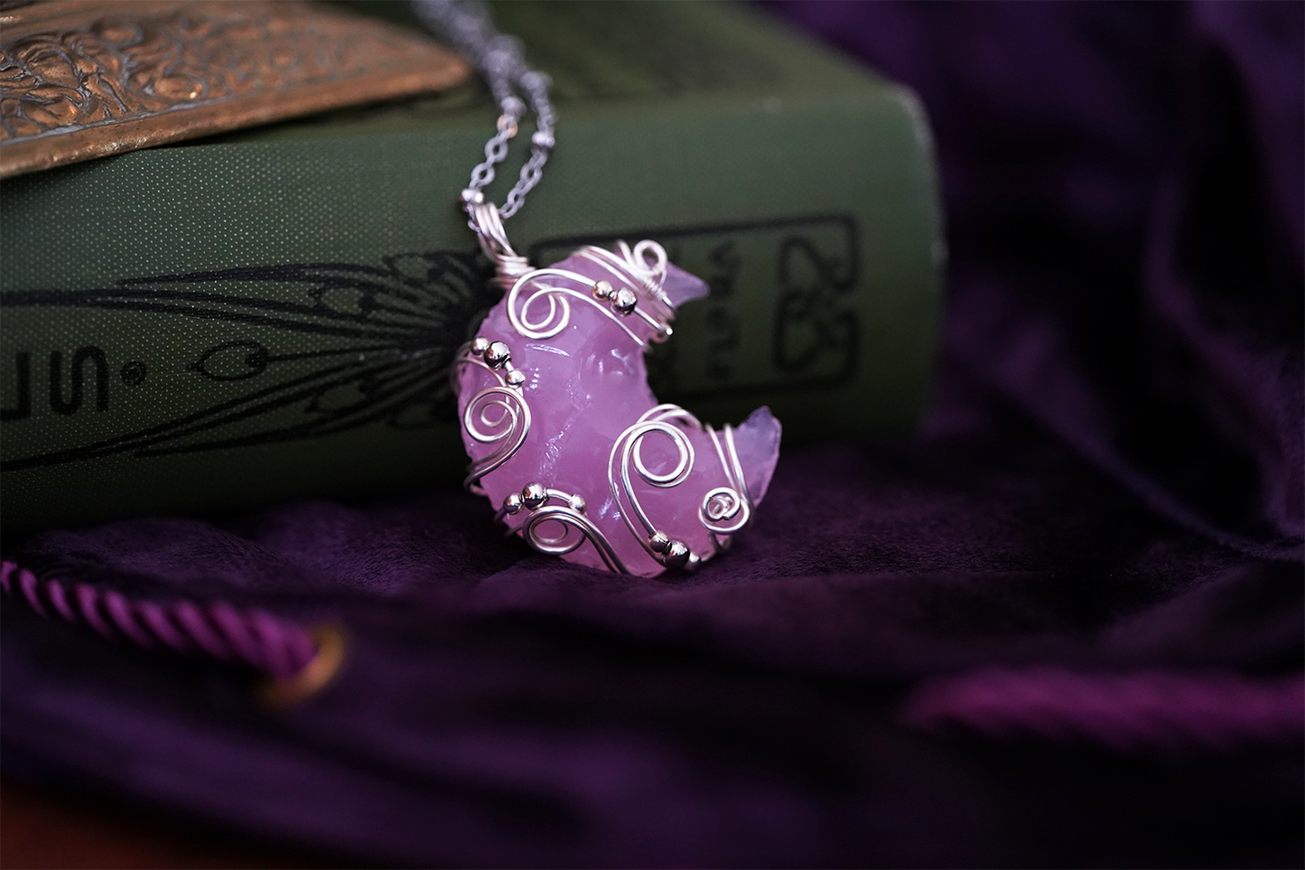 Pink, rose quartz crescent moon necklace on a purple fabric background